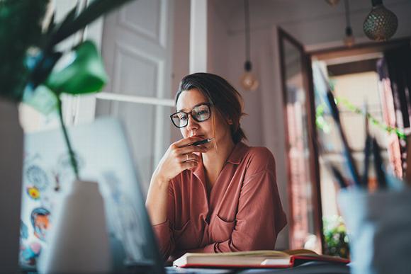 lady sitting at home with pen in hand looking in concentration at laptop on table